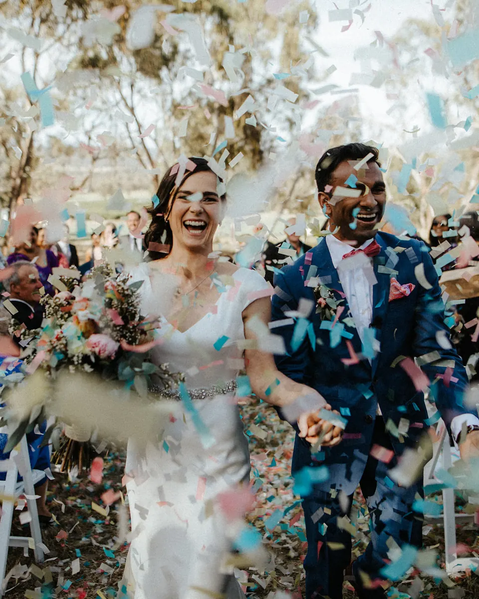 A couple leaving their ceremony through cheering guests and confetti